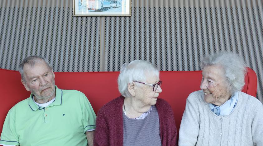 Ein älterer Herr und zwei ältere Damen sitzen nebeneinander auf einem Sofa.