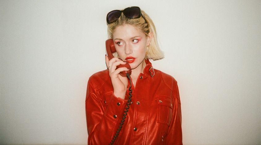 Yeva in einer auffälligen Roten Jacke hält ein rotes Kabeltelefon an ihr Ohr.