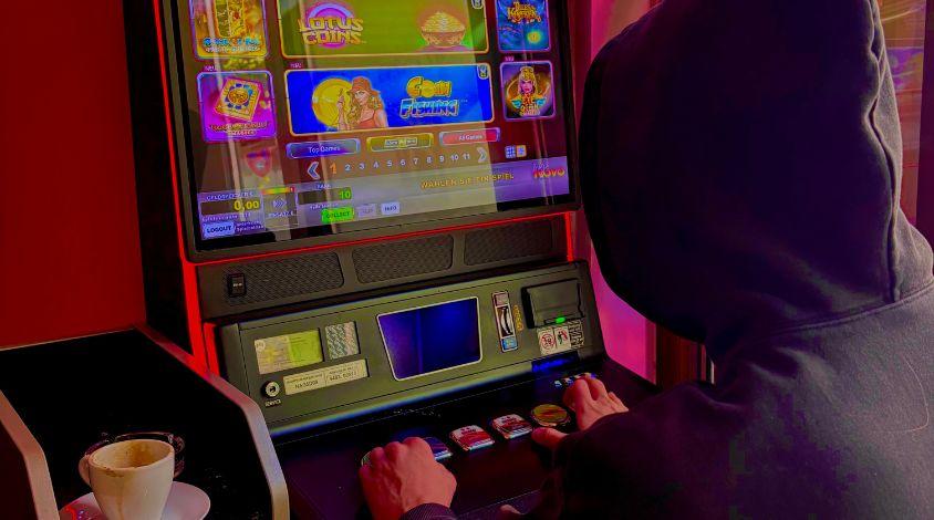 Mann mit schwarzer Kapuze vor Spielautomaten