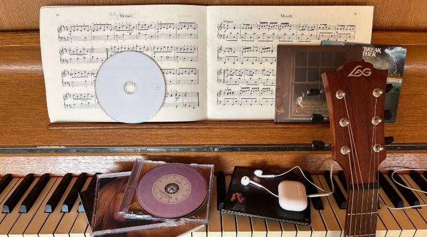 Ein Klavier auf dem verschiedene CDs liegen sowie Kopfhörer und man sieht den Kopf einer Gitarre.