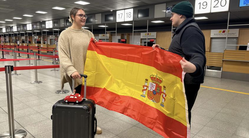Mit Koffer, Sparschwein und Spanienflagge am Flughafen