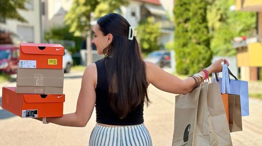 Junge Frau mit Einkaufstaschen und Schuhkartons nach einem Shoppingtrip. Das Bild symbolisiert Konsum und Retail Therapy.
